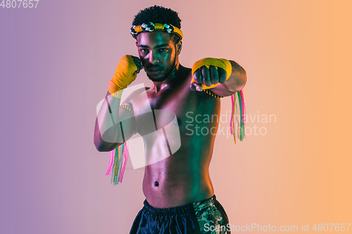 Image of Muay thai. Young man exercising thai boxing on gradient background