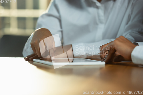 Image of Close up of african-american human\'s hands using tablet on wooden table