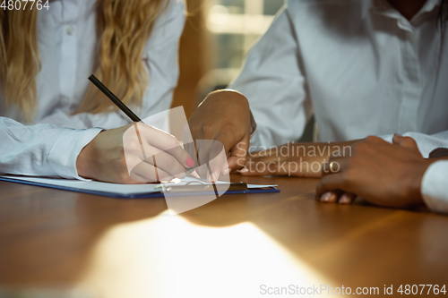 Image of Close up of african-american and caucasian human\'s hands writing on sheets on wooden table