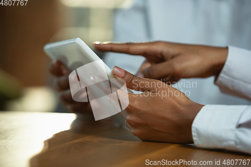 Image of Close up of african-american human\'s hands using tablet on wooden table