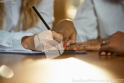 Image of Close up of african-american and caucasian human\'s hands writing on sheets on wooden table