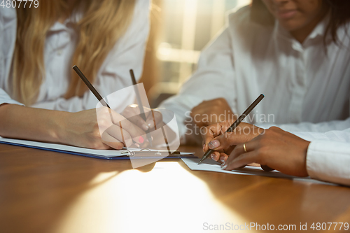 Image of Close up of african-american and caucasian human\'s hands writing on sheets on wooden table