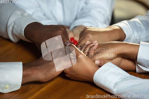 Image of Close up of african-american and caucasian human\'s hands holding on wooden table