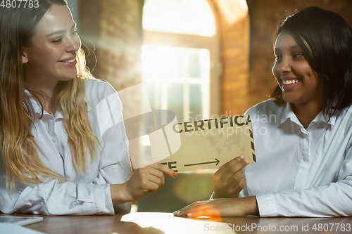 Image of Close up of african-american and caucasian human\'s hands holding certificate or inviting card