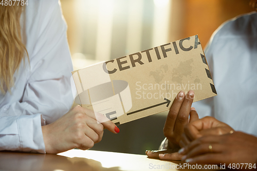 Image of Close up of african-american and caucasian human\'s hands holding certificate or inviting card