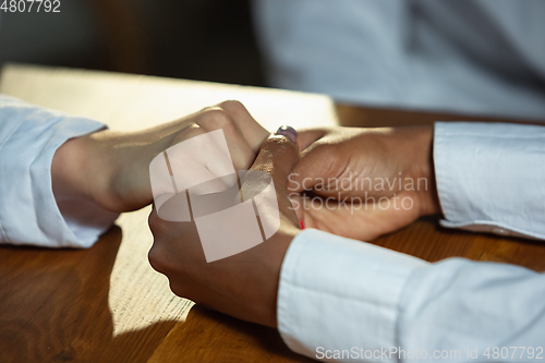Image of Close up of african-american and caucasian human\'s hands holding on wooden table