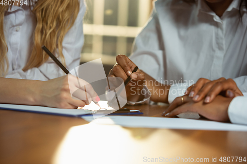 Image of Close up of african-american and caucasian human\'s hands writing on sheets on wooden table