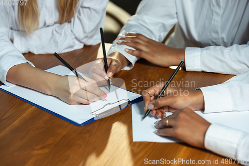 Image of Close up of african-american and caucasian human\'s hands writing on sheets on wooden table