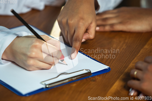 Image of Close up of african-american and caucasian human\'s hands writing on sheets on wooden table