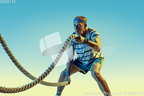 Image of Senior man training with ropes in sportwear on gradient background and neon light