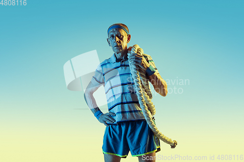 Image of Senior man training with ropes in sportwear on gradient background and neon light