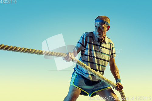 Image of Senior man training with ropes in sportwear on gradient background and neon light