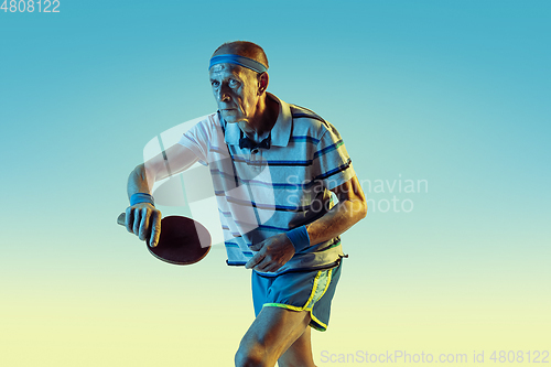 Image of Senior man playing table tennis in sportwear on gradient background and neon light