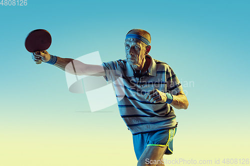 Image of Senior man playing table tennis in sportwear on gradient background and neon light