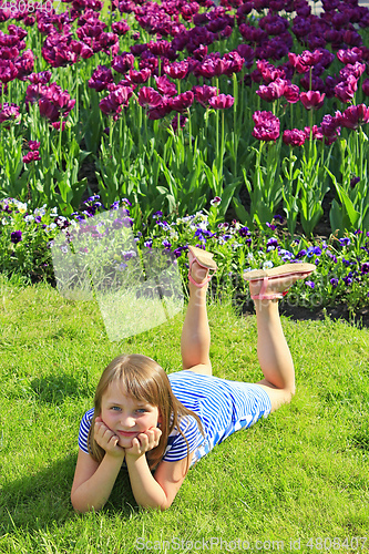 Image of little girl lies on the grass near the tulips
