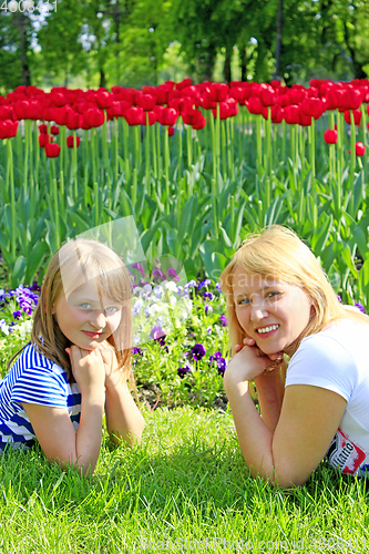Image of little girl and her mother lay on the grass near the tulips
