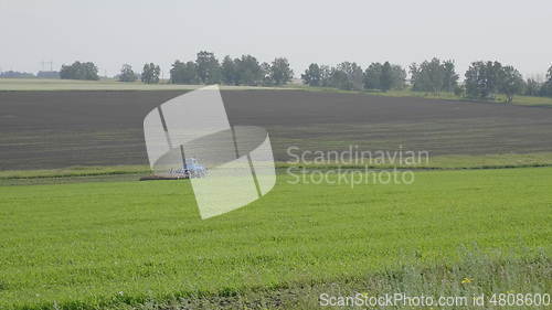 Image of Blue wheeled tractor plowing a green field