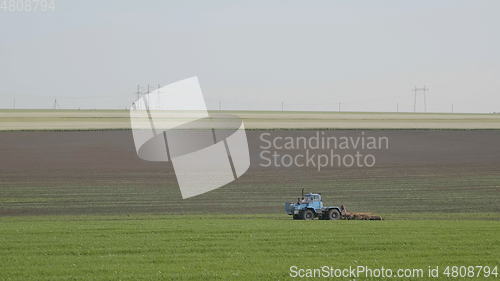 Image of Blue wheeled tractor plowing a green field