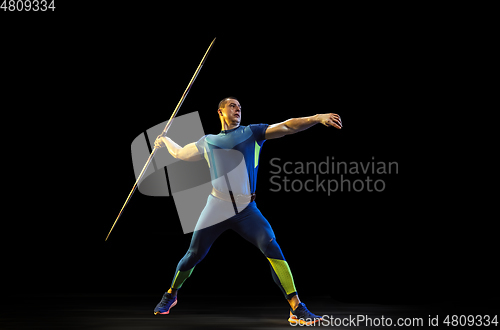 Image of Male athlete practicing in throwing javelin isolated on black studio background in neon light