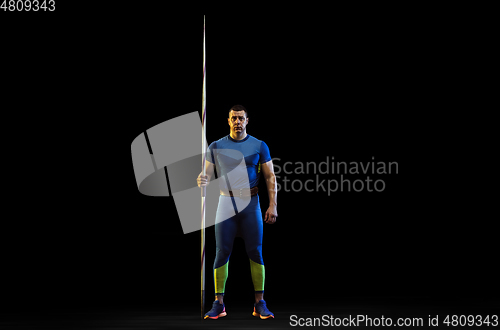 Image of Male athlete practicing in throwing javelin isolated on black studio background in neon light