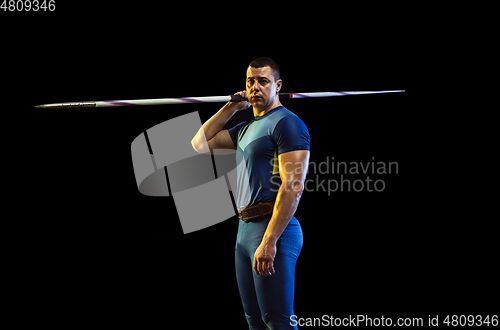 Image of Male athlete practicing in throwing javelin isolated on black studio background in neon light