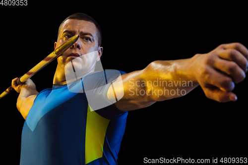 Image of Male athlete practicing in throwing javelin isolated on black studio background in neon light