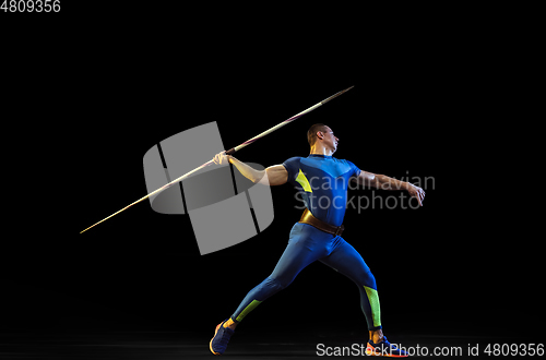 Image of Male athlete practicing in throwing javelin isolated on black studio background in neon light