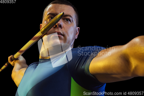 Image of Male athlete practicing in throwing javelin isolated on black studio background in neon light