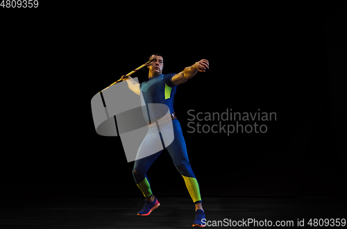 Image of Male athlete practicing in throwing javelin isolated on black studio background in neon light