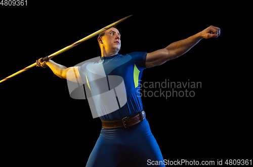 Image of Male athlete practicing in throwing javelin isolated on black studio background in neon light