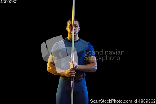 Image of Male athlete practicing in throwing javelin isolated on black studio background in neon light