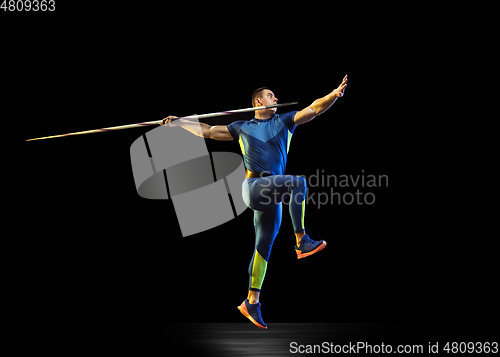 Image of Male athlete practicing in throwing javelin isolated on black studio background in neon light