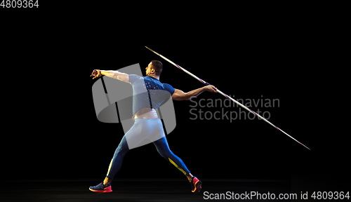 Image of Male athlete practicing in throwing javelin isolated on black studio background in neon light