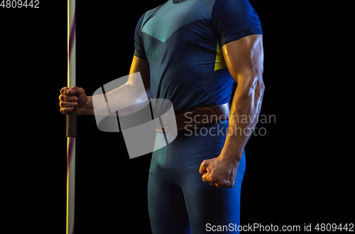 Image of Male athlete practicing in throwing javelin isolated on black studio background in neon light