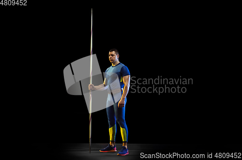 Image of Male athlete practicing in throwing javelin isolated on black studio background in neon light