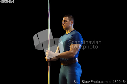 Image of Male athlete practicing in throwing javelin isolated on black studio background in neon light