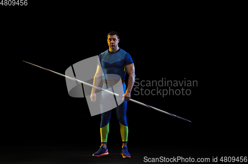 Image of Male athlete practicing in throwing javelin isolated on black studio background in neon light