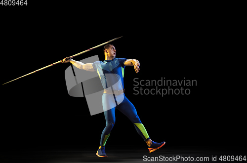 Image of Male athlete practicing in throwing javelin isolated on black studio background in neon light