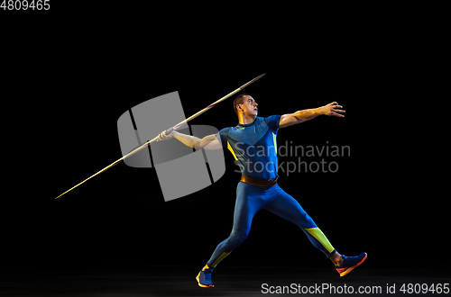 Image of Male athlete practicing in throwing javelin isolated on black studio background in neon light