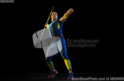 Image of Male athlete practicing in throwing javelin isolated on black studio background in neon light