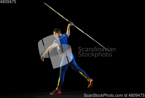 Image of Male athlete practicing in throwing javelin isolated on black studio background in neon light