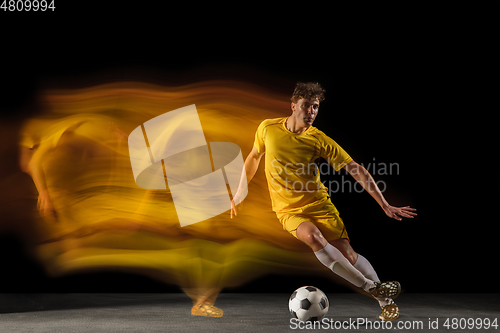 Image of Young caucasian male football or soccer player kicking ball for the goal in mixed light on dark background. Concept of healthy lifestyle, professional sport, hobby.