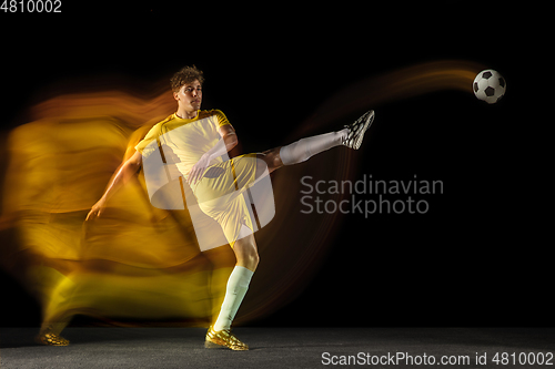 Image of Young caucasian male football or soccer player kicking ball for the goal in mixed light on dark background. Concept of healthy lifestyle, professional sport, hobby.