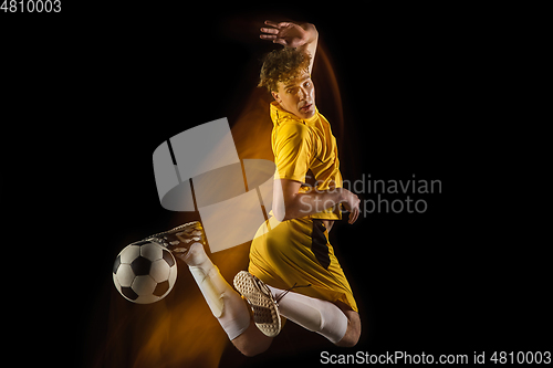 Image of Young caucasian male football or soccer player kicking ball for the goal in mixed light on dark background. Concept of healthy lifestyle, professional sport, hobby.