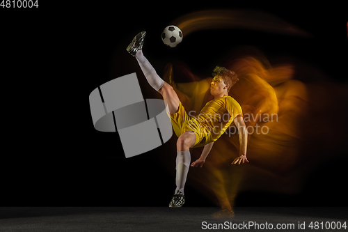 Image of Young caucasian male football or soccer player kicking ball for the goal in mixed light on dark background. Concept of healthy lifestyle, professional sport, hobby.