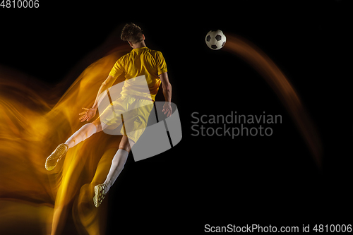 Image of Young caucasian male football or soccer player kicking ball for the goal in mixed light on dark background. Concept of healthy lifestyle, professional sport, hobby.