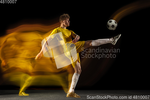 Image of Young caucasian male football or soccer player kicking ball for the goal in mixed light on dark background. Concept of healthy lifestyle, professional sport, hobby.