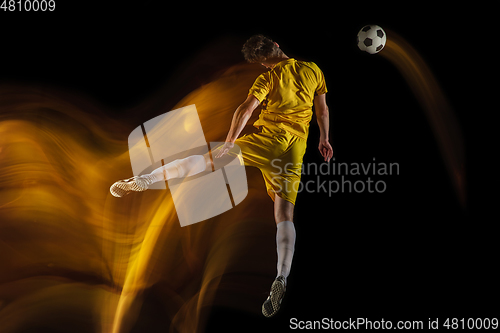 Image of Young caucasian male football or soccer player kicking ball for the goal in mixed light on dark background. Concept of healthy lifestyle, professional sport, hobby.