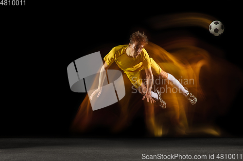 Image of Young caucasian male football or soccer player kicking ball for the goal in mixed light on dark background. Concept of healthy lifestyle, professional sport, hobby.