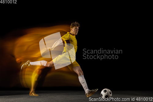 Image of Young caucasian male football or soccer player kicking ball for the goal in mixed light on dark background. Concept of healthy lifestyle, professional sport, hobby.